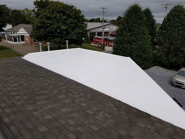 Roof with dark shingles beside a newly coated white roof section, viewed from above.