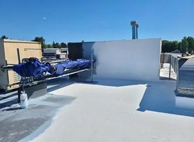 Flat white rooftop with HVAC units and a blue tarp-covered object under a clear sky