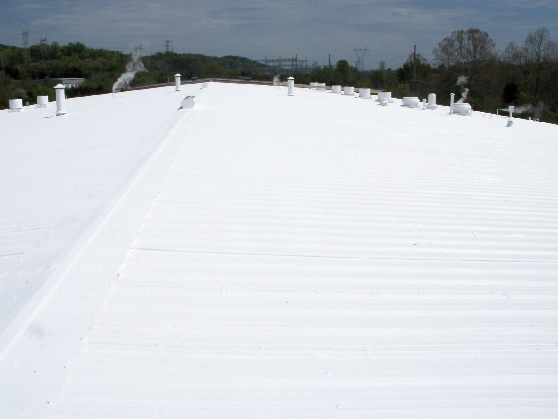 White flat rooftop with several vents under a cloudy sky