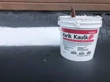 White Kwik Kaulk bucket on a dark roof with a trowel sticking out