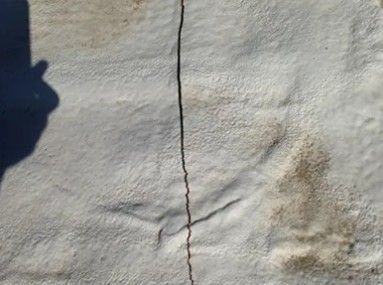 Close-up of a white textured wall with a vertical crack and a small brown stain