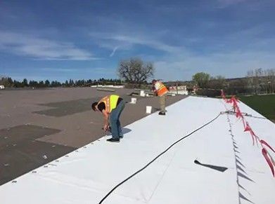 Worker bending on a white rooftop under a blue sky, with safety lines and materials nearby