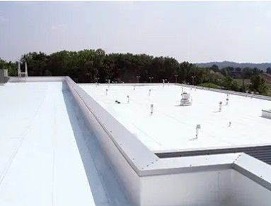 White flat rooftop with vents and a raised edge, overlooking trees and distant hills