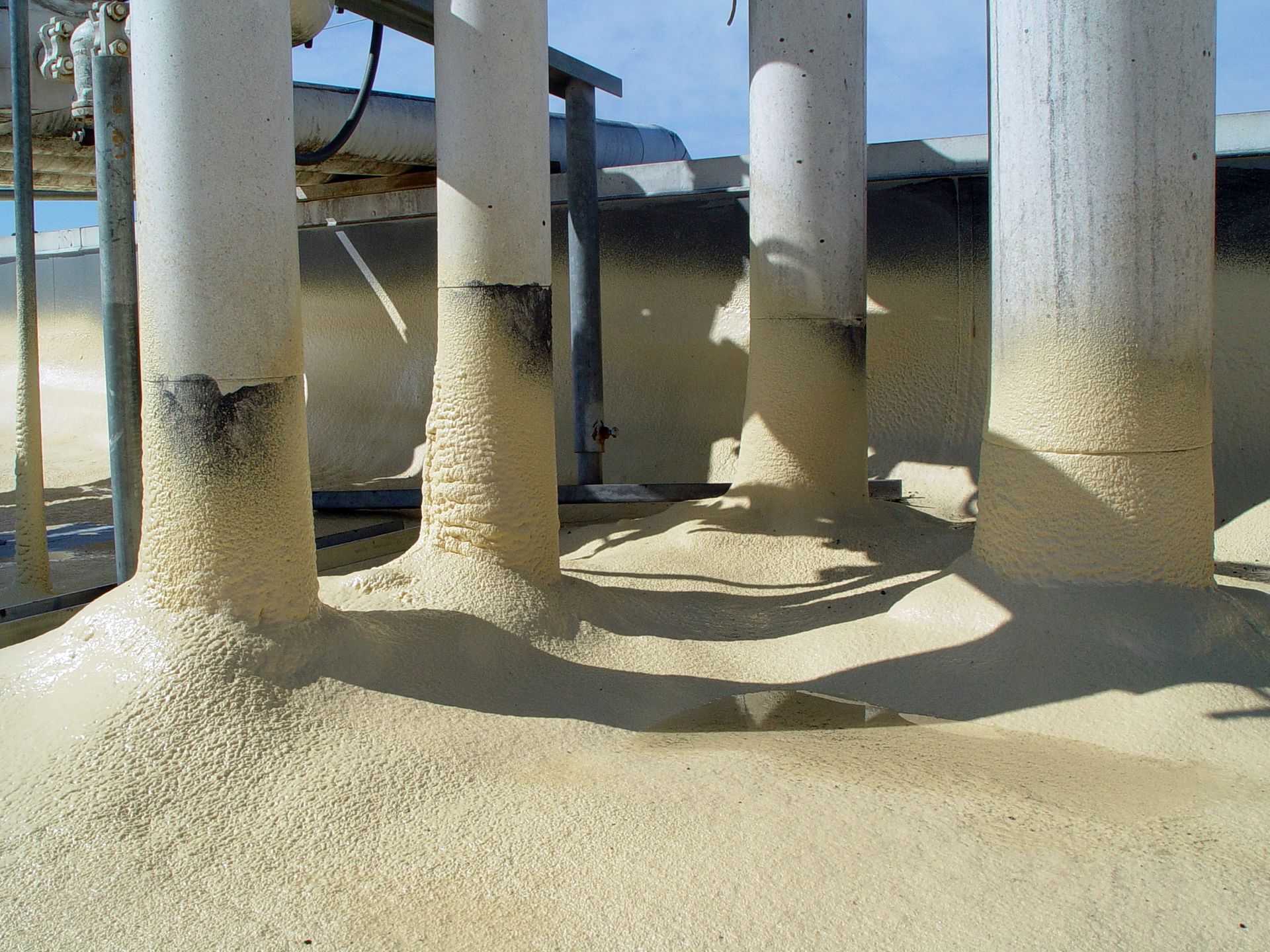 Sand piled around white support columns beneath an elevated structure, with blue sky in the background