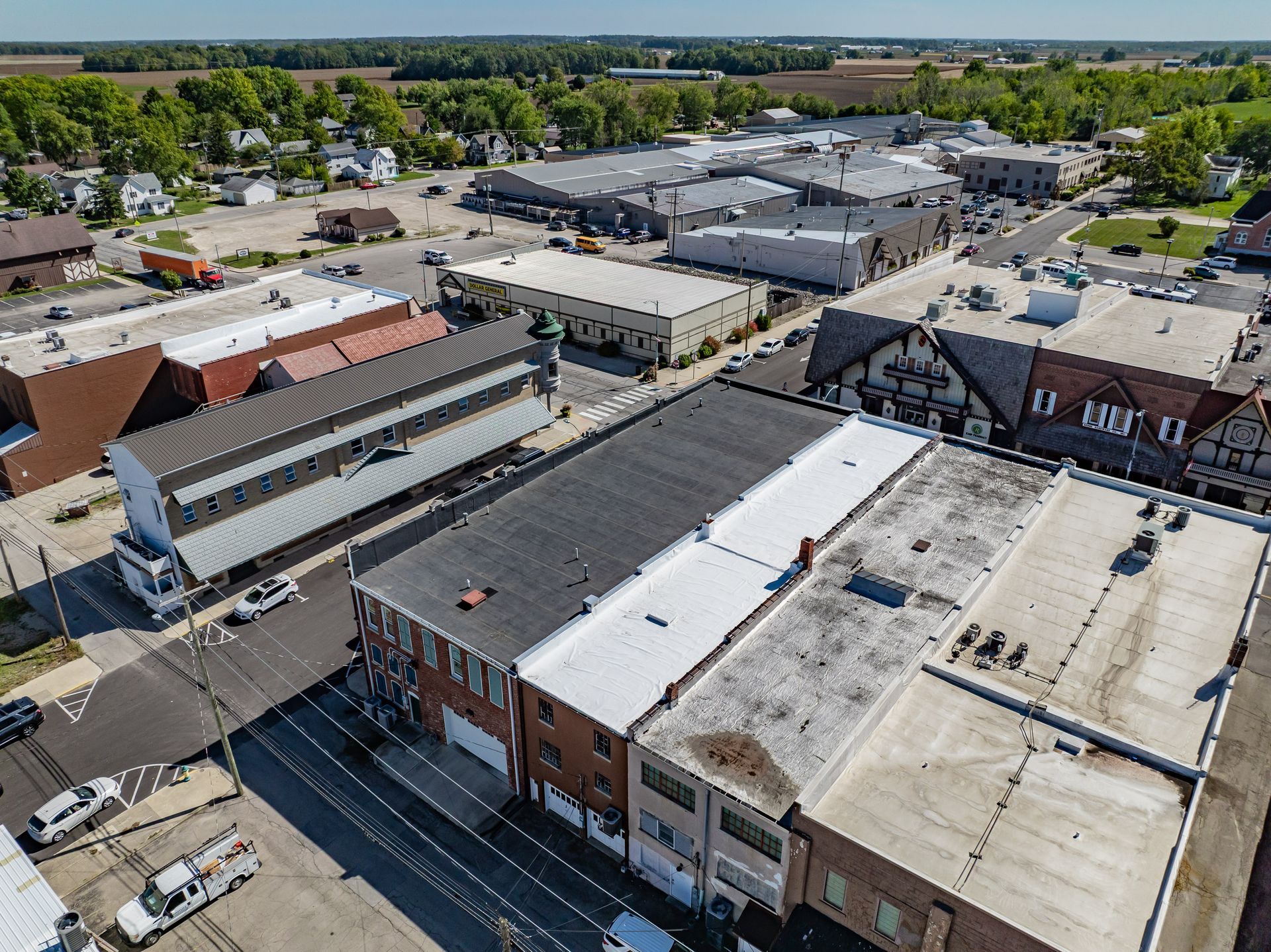 Aerial view of a small downtown with brick rooftops, parking lots, and tree-lined streets under a clear sky