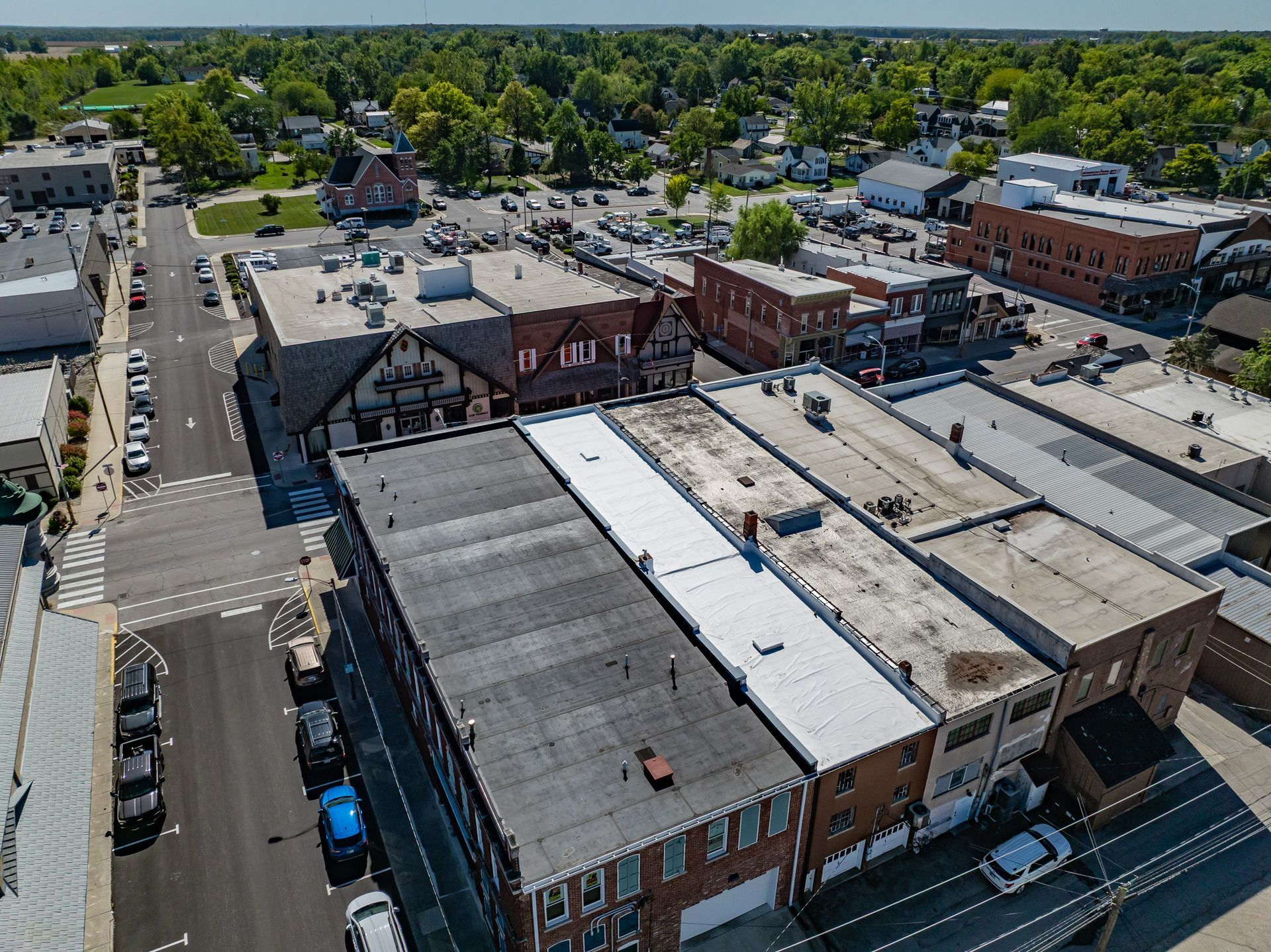 Aerial view of a small downtown with brick buildings, streets, and parked cars under a sunny sky