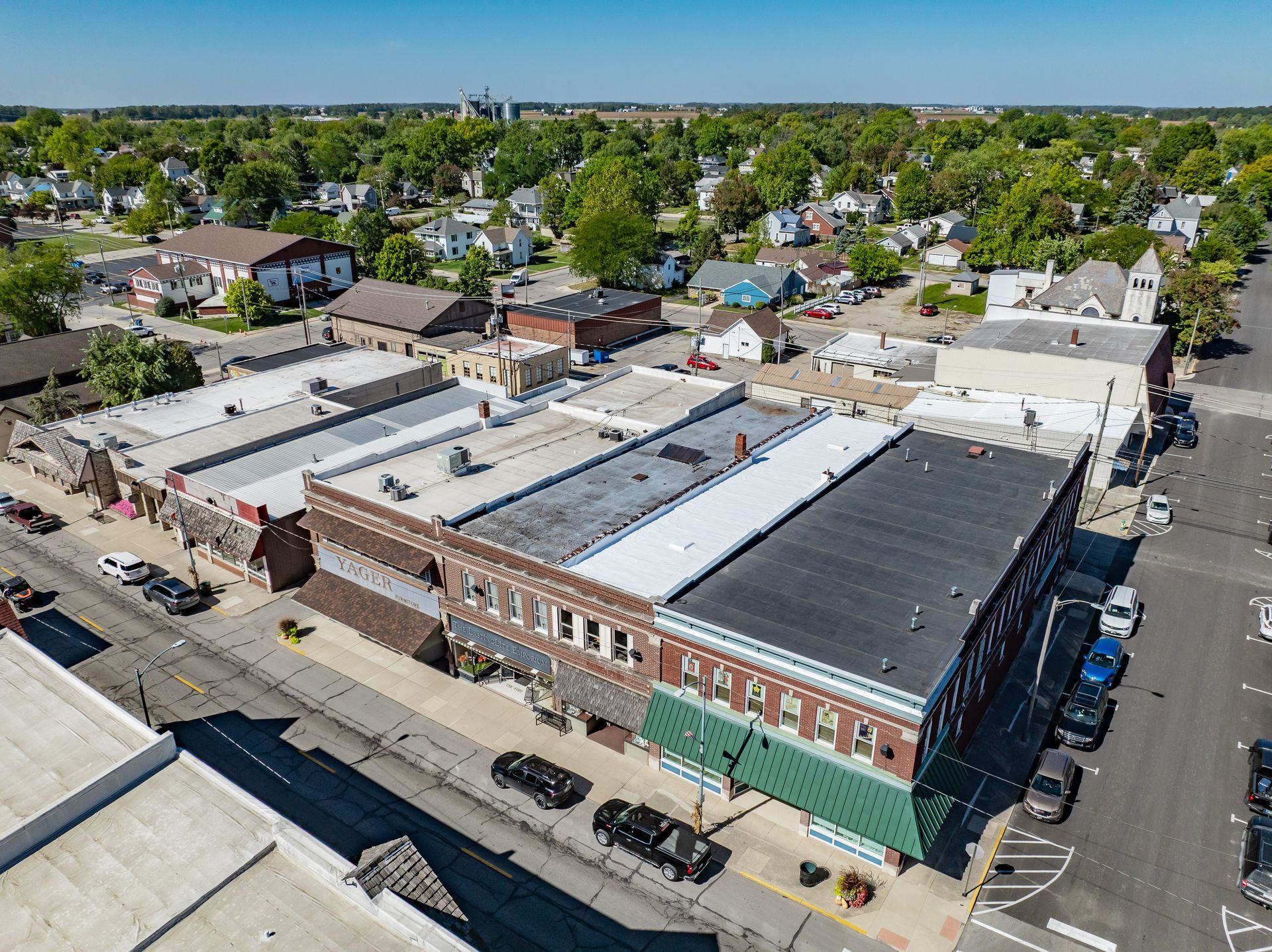 Aerial view of a small downtown block with brick buildings, parked cars, and tree-lined streets