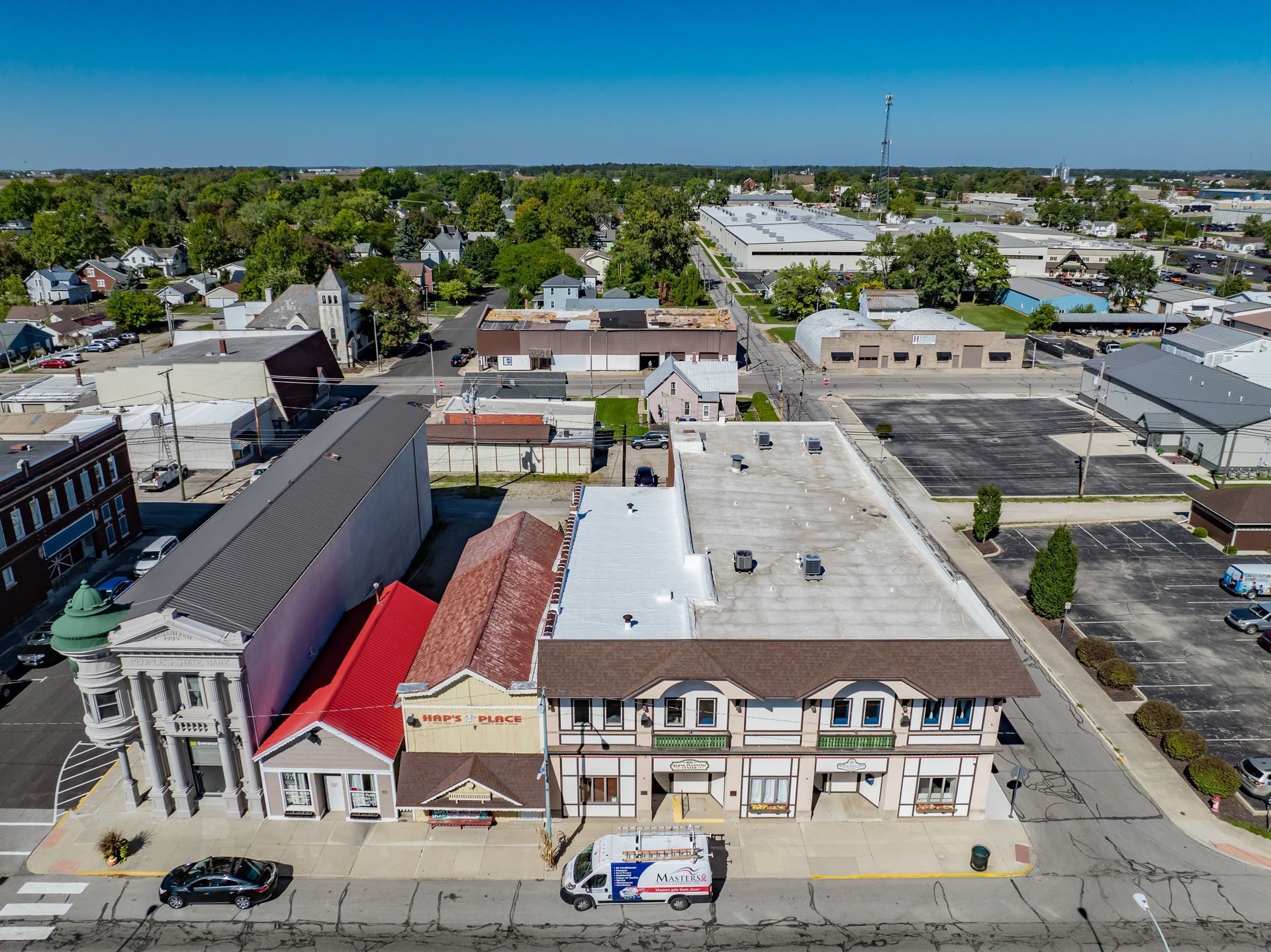 Aerial view of a small downtown with storefronts, parked cars, and low-rise buildings on a sunny day