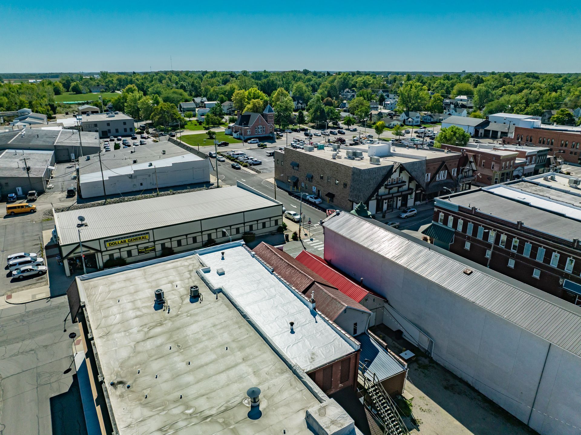Aerial view of low-rise downtown buildings with rooftops, trees, and a clear blue sky.