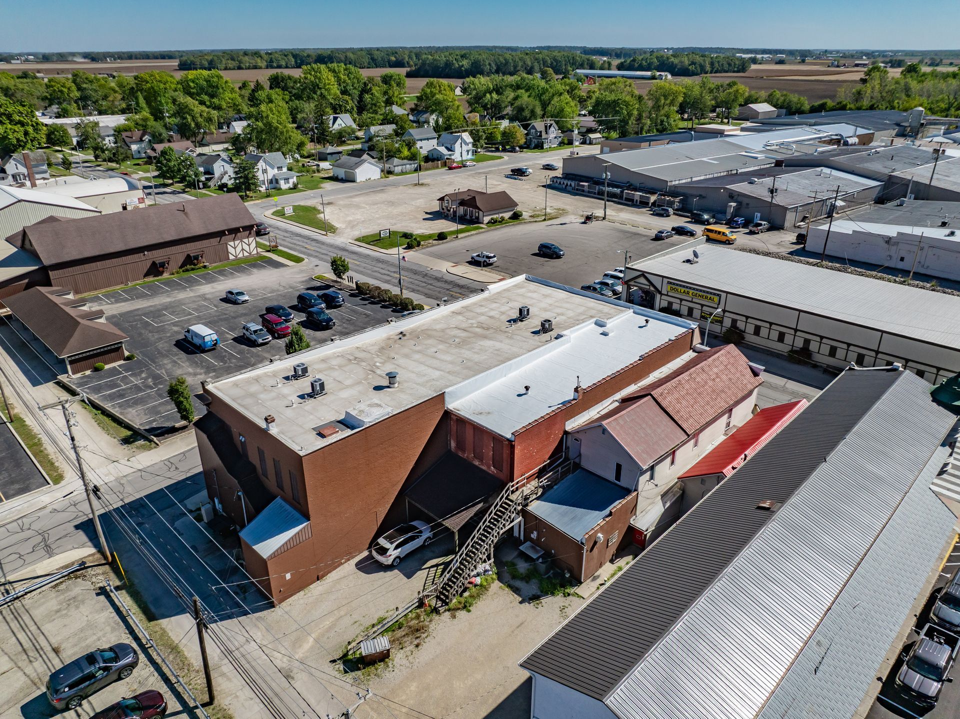 Aerial view of a brick commercial building with parking lots and surrounding businesses on a sunny day