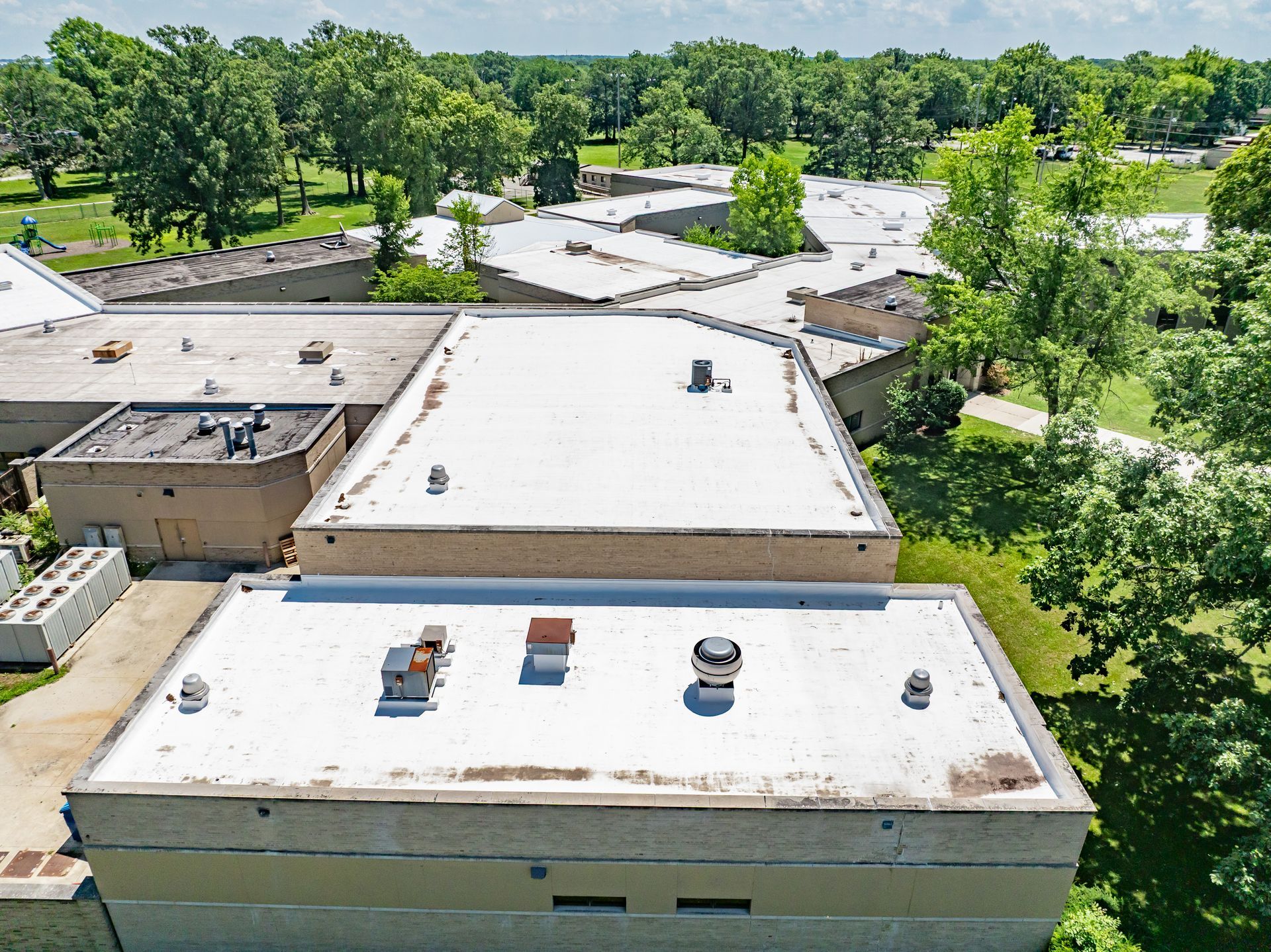 Aerial view of flat-roof buildings surrounded by trees in a green suburban area
