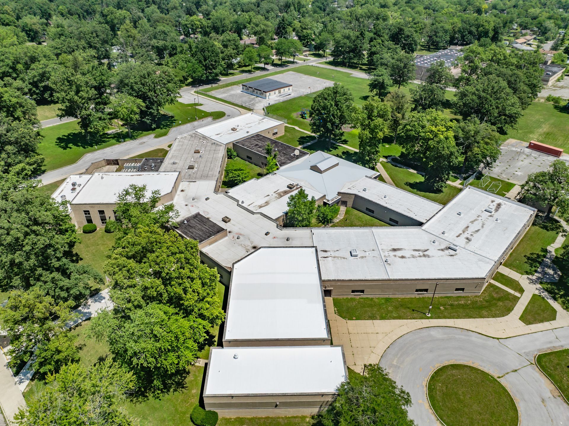 Aerial view of a low-rise school campus with white-roofed buildings surrounded by trees and lawns