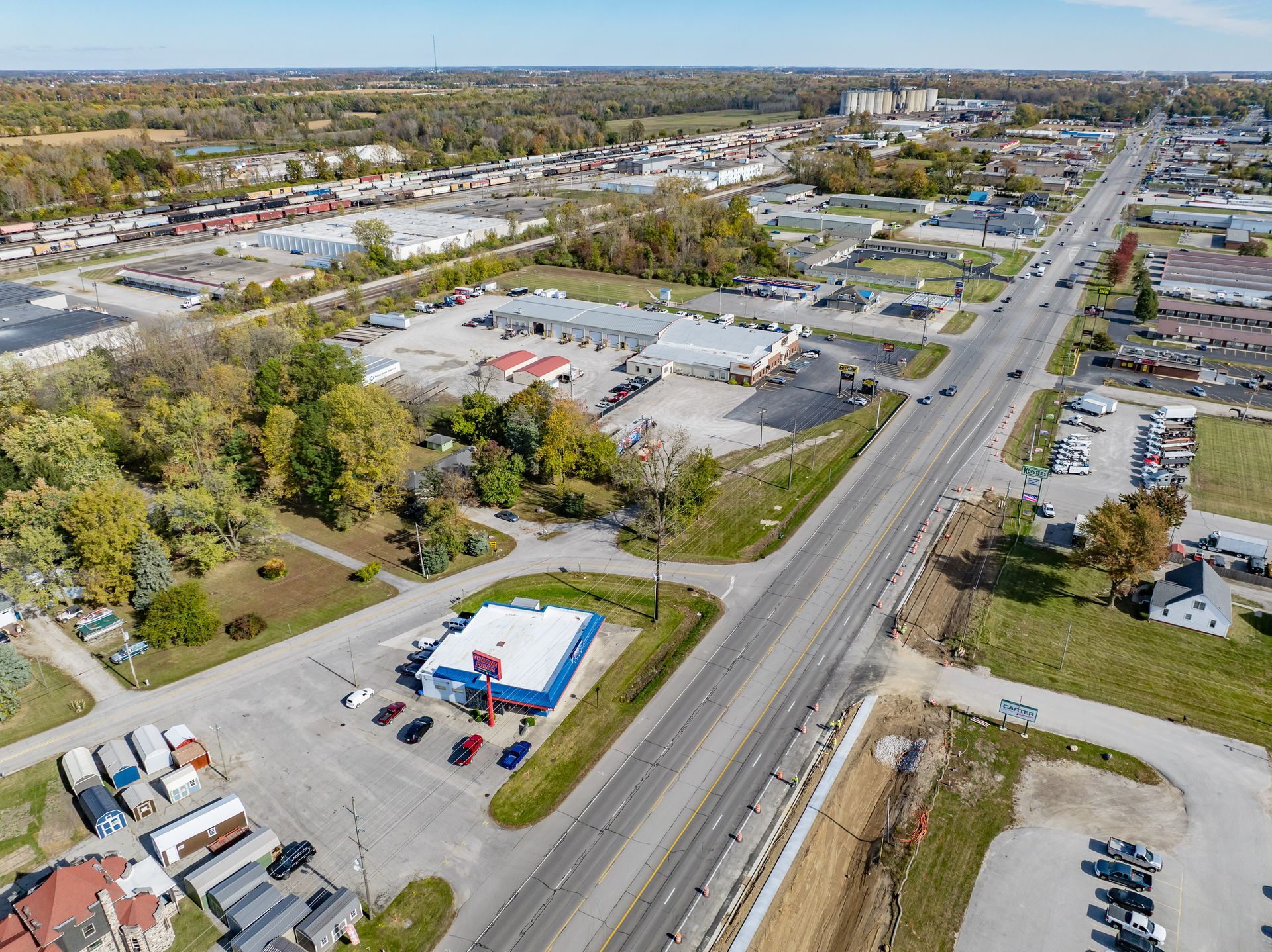 Aerial view of a suburban shopping area with roads, parking lots, and scattered buildings in fall.