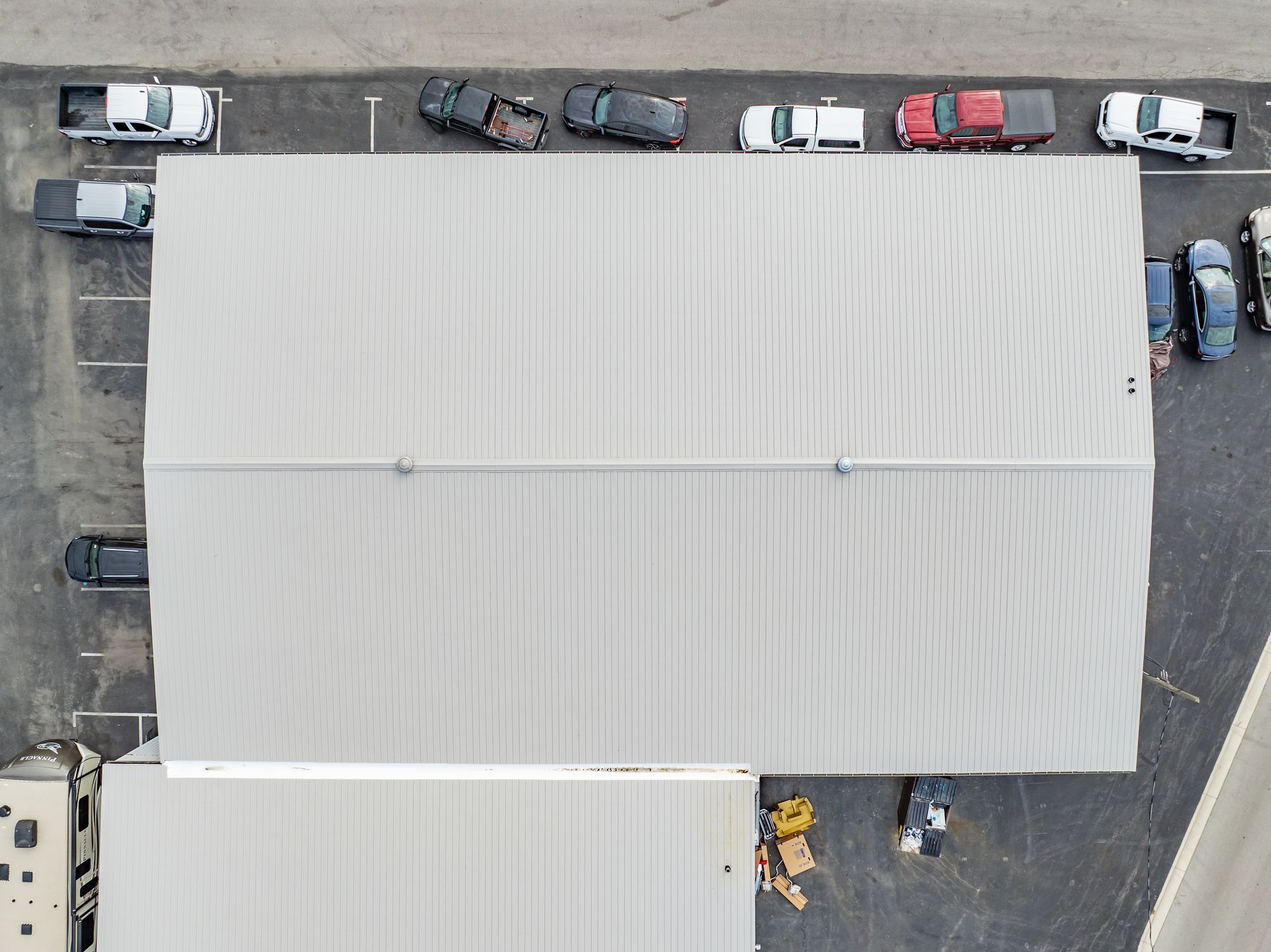 Aerial view of a large white-roofed building surrounded by parked cars and trucks in a lot.