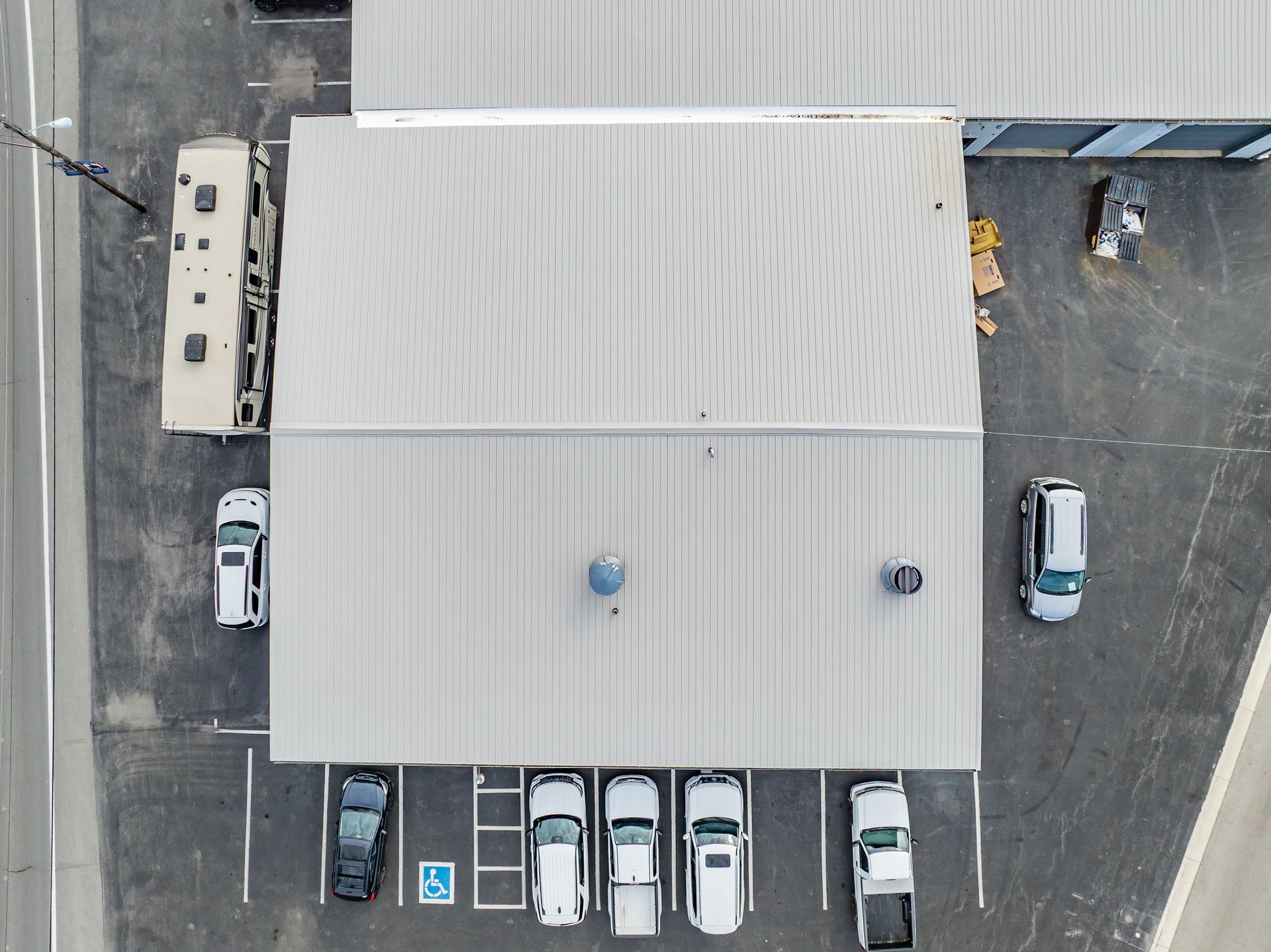 Aerial view of a large gray-roofed building with parked cars around it in a parking lot.