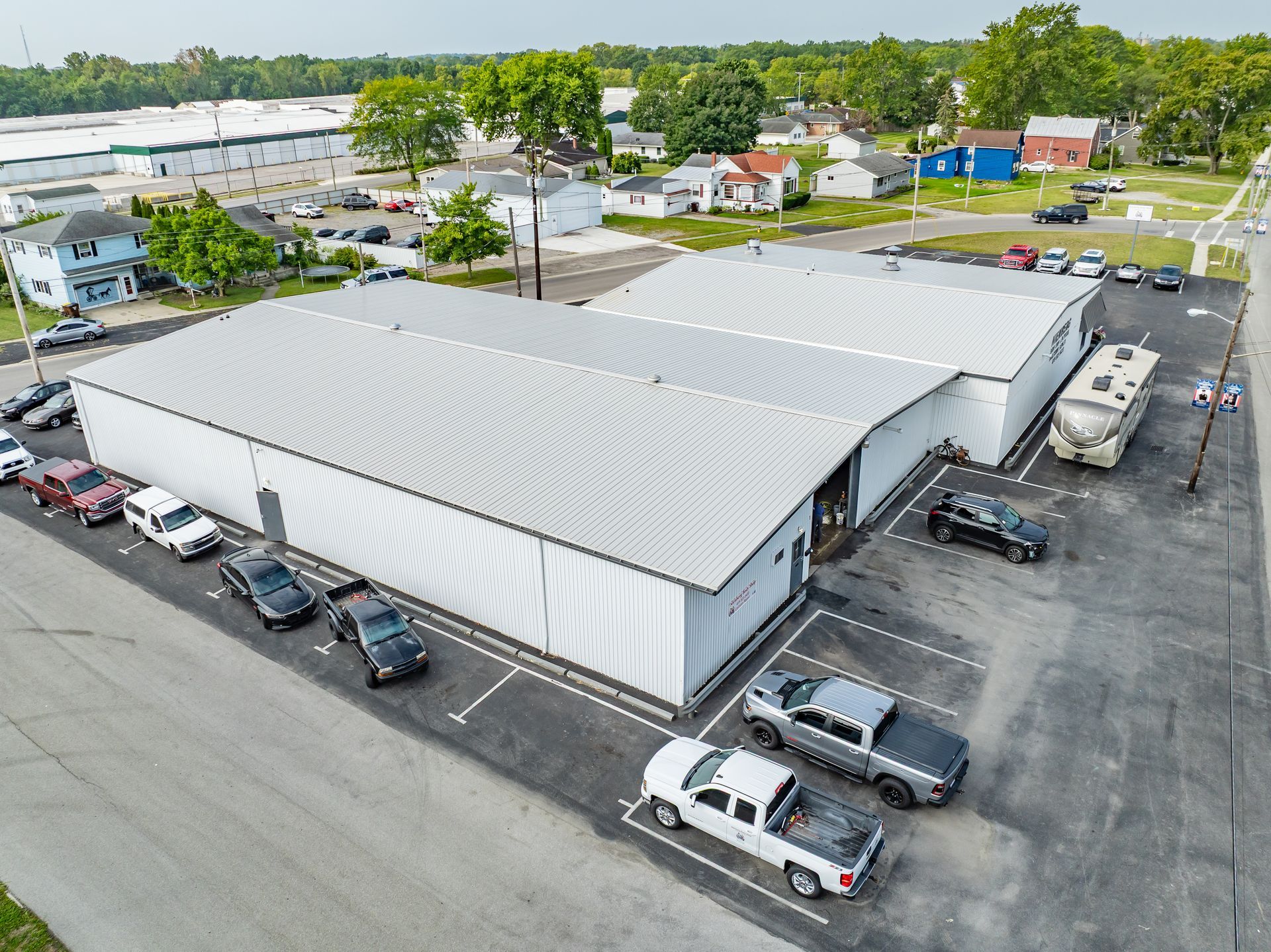 Aerial view of a large white industrial building with parked cars in a lot.