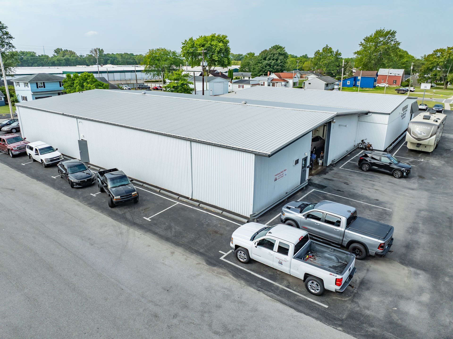 White warehouse building with parked cars and pickup trucks in an industrial lot