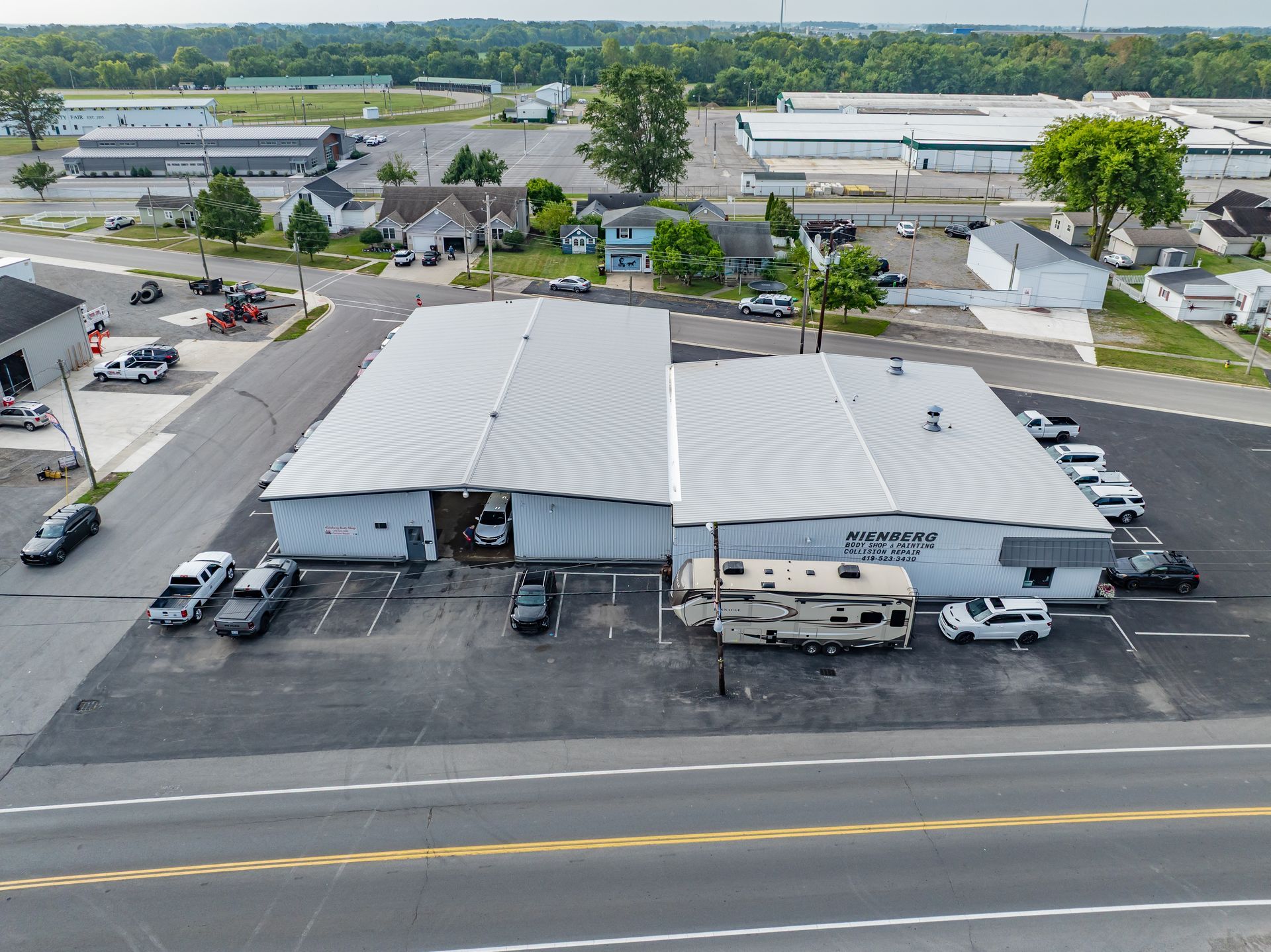 Aerial view of a white warehouse with parked cars beside a road in an industrial area