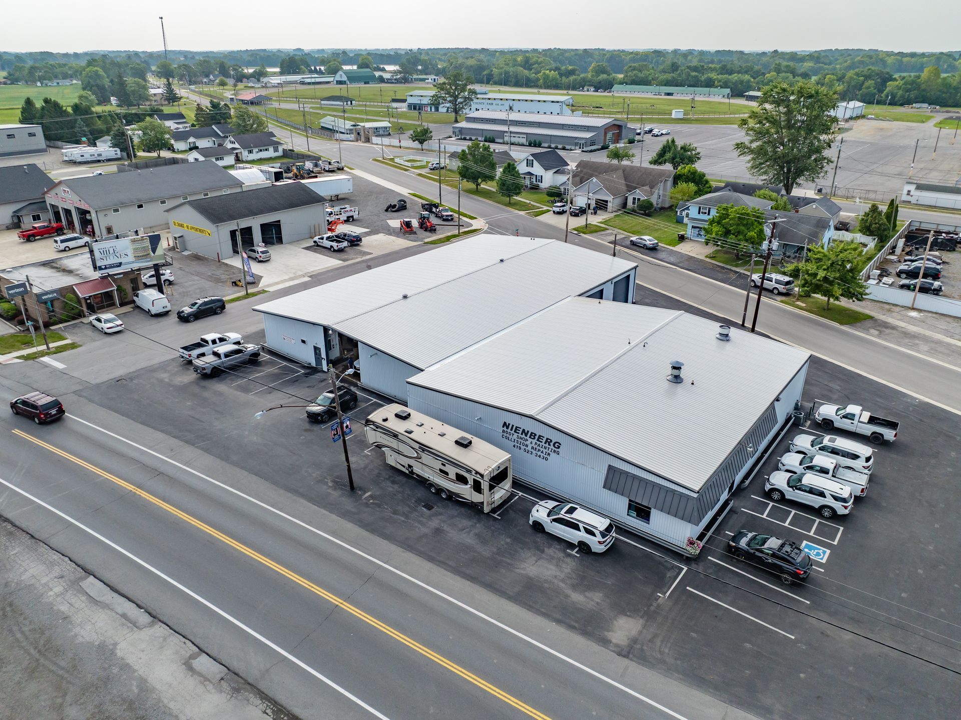 Aerial view of a white-roofed gas station and convenience store with cars parked along a busy road.