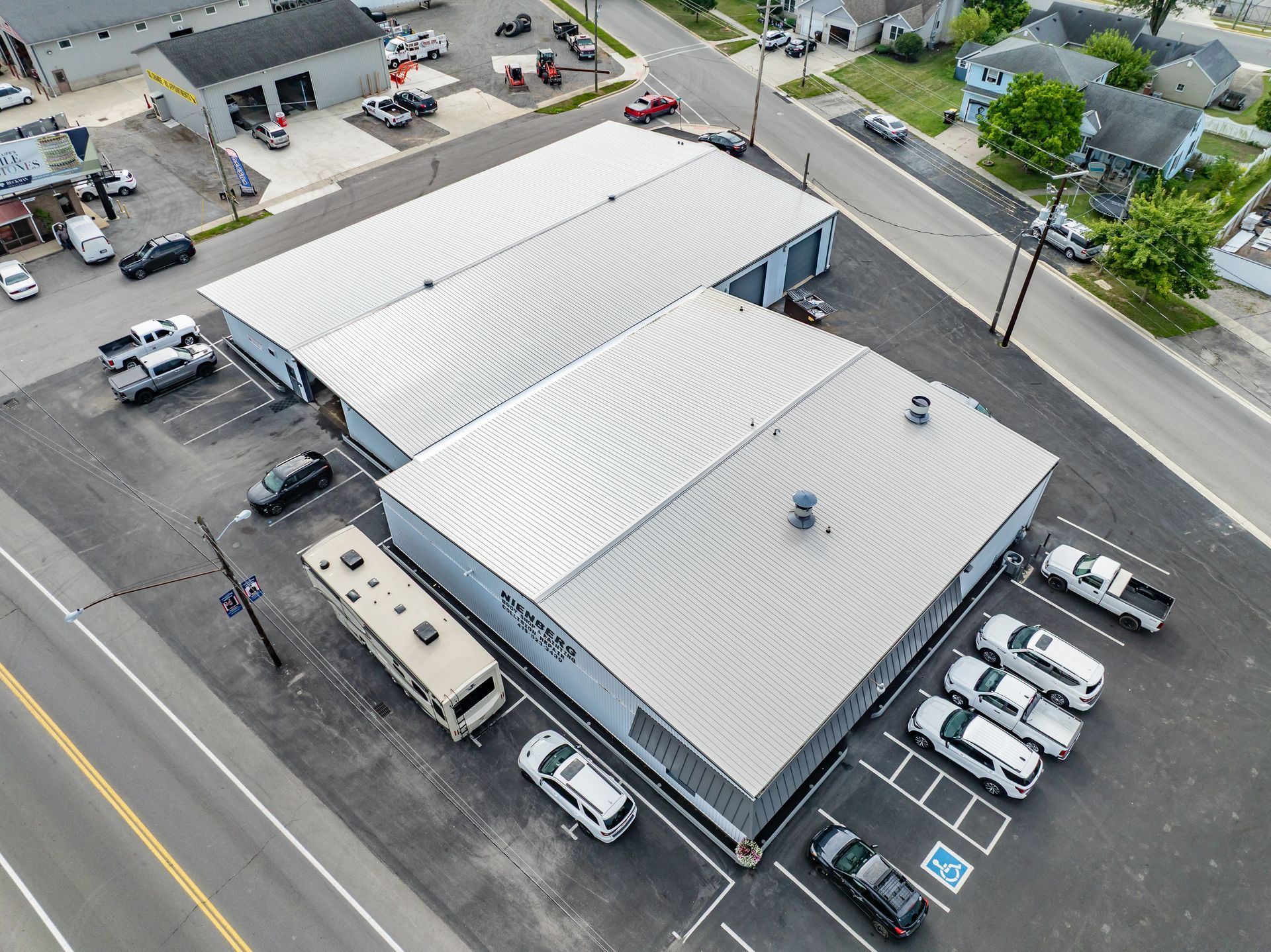 Aerial view of a commercial building with white roofs, parked vehicles, and surrounding streets.