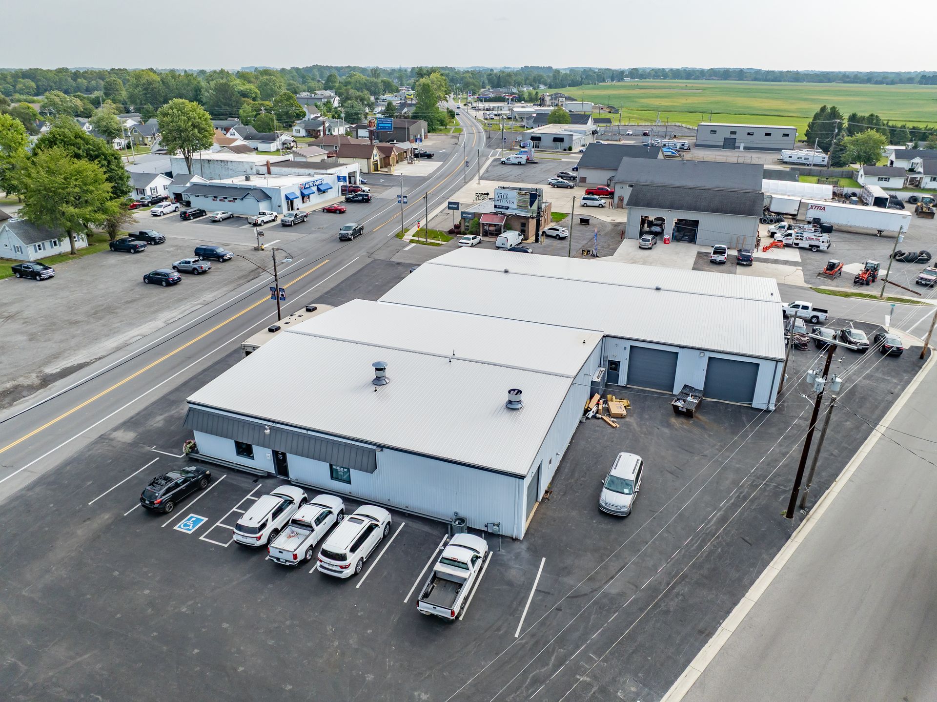 Aerial view of a commercial building with parked cars and nearby roads in a small town.