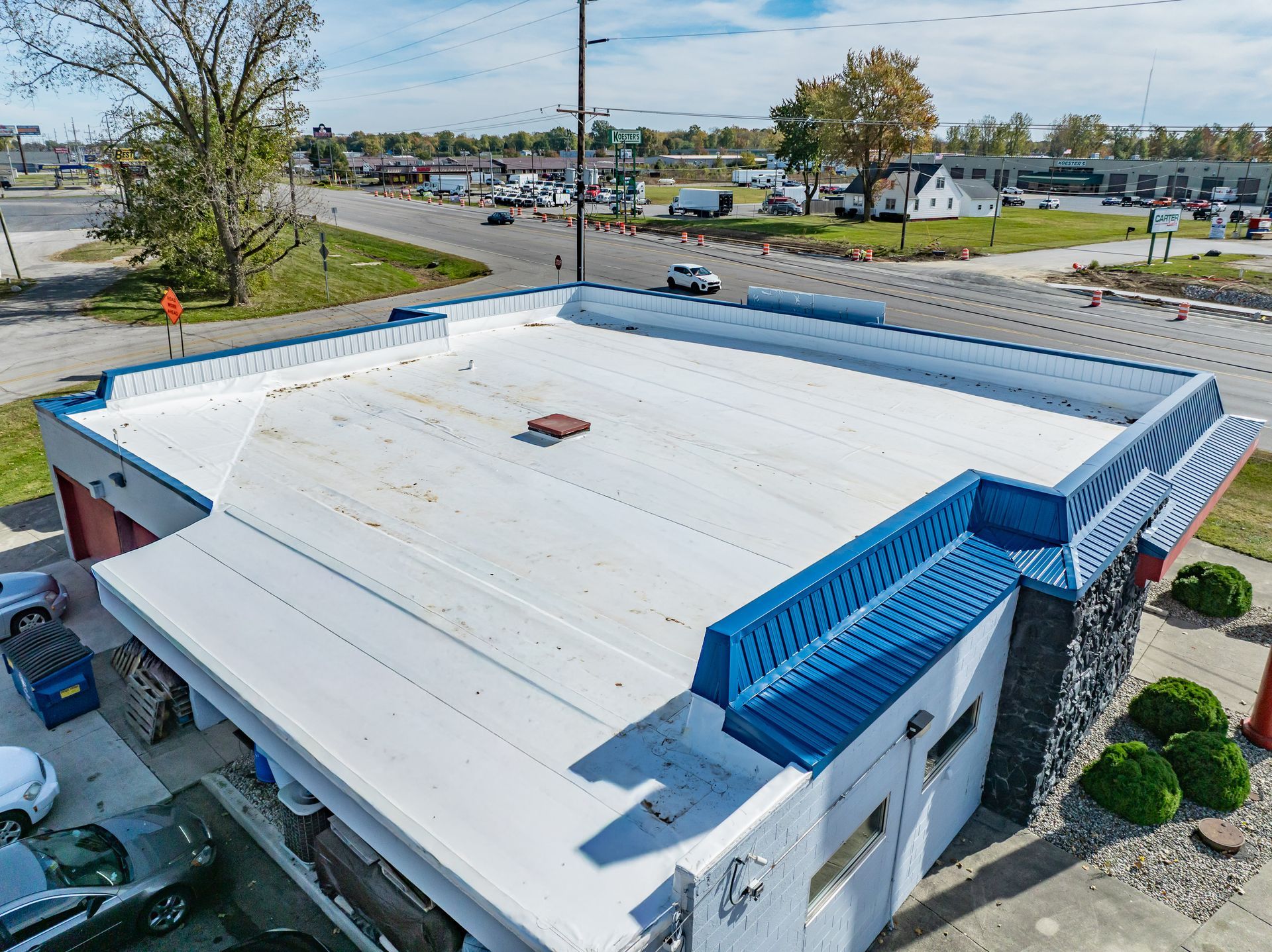 Aerial view of a white-roofed building with blue trim beside a road and parking lot.