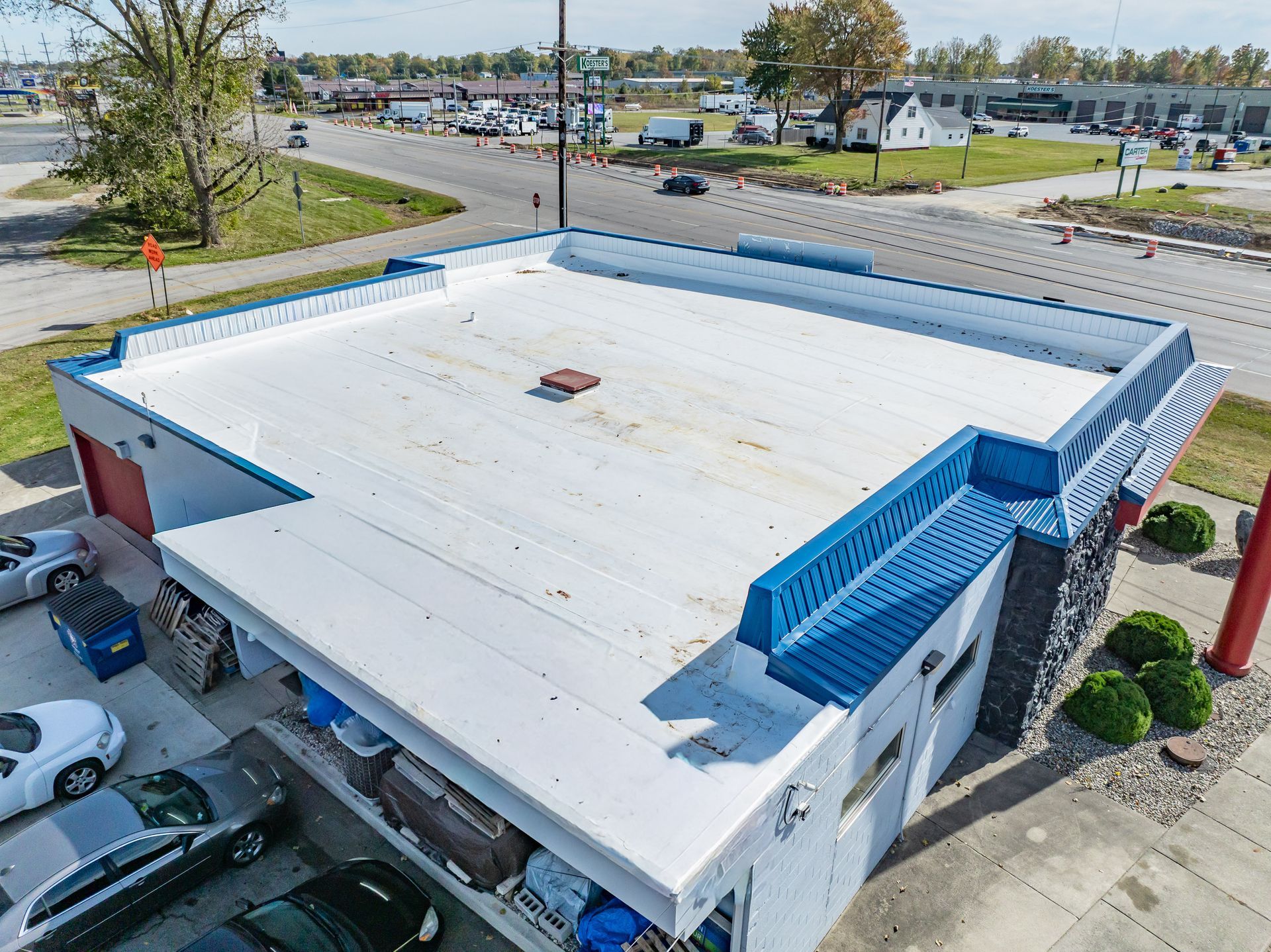 Aerial view of a white-roofed building with blue awnings and a parking lot nearby.