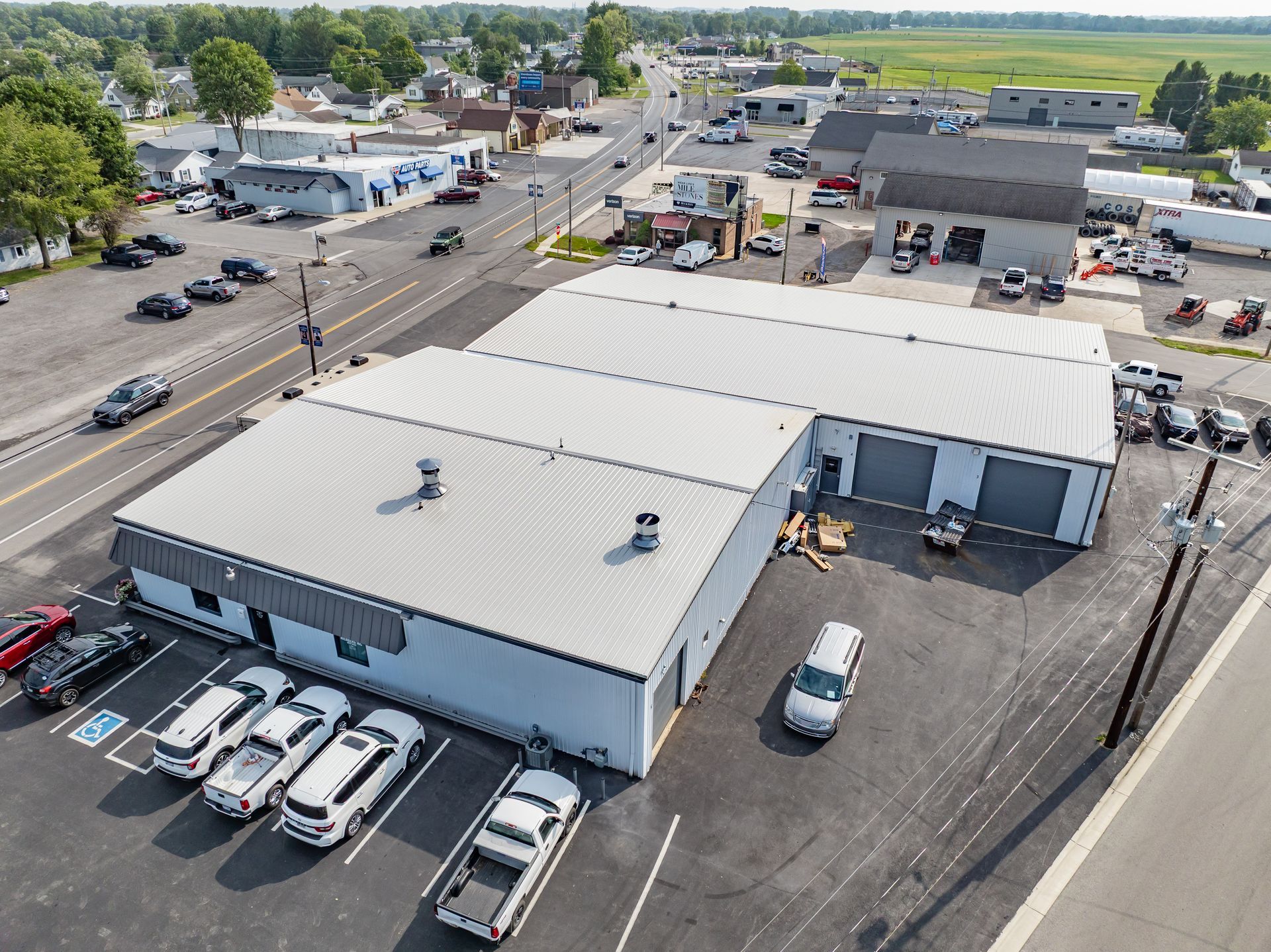 Aerial view of a white industrial building with parked cars, nearby road, and surrounding businesses.