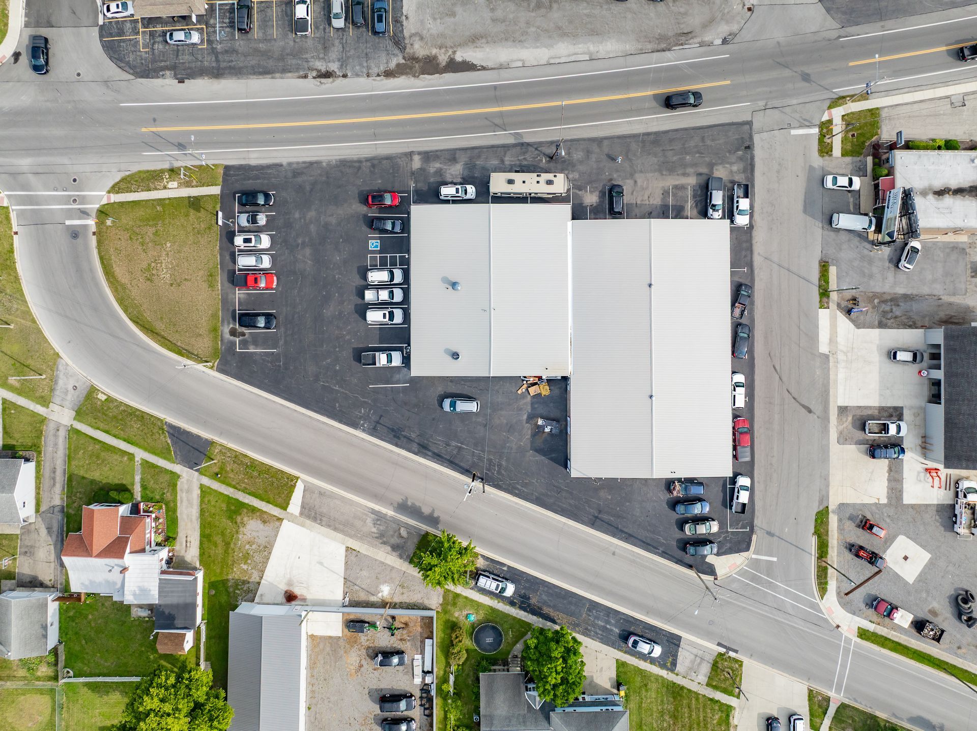 Aerial view of a parking lot beside a large gray-roofed building and curved road