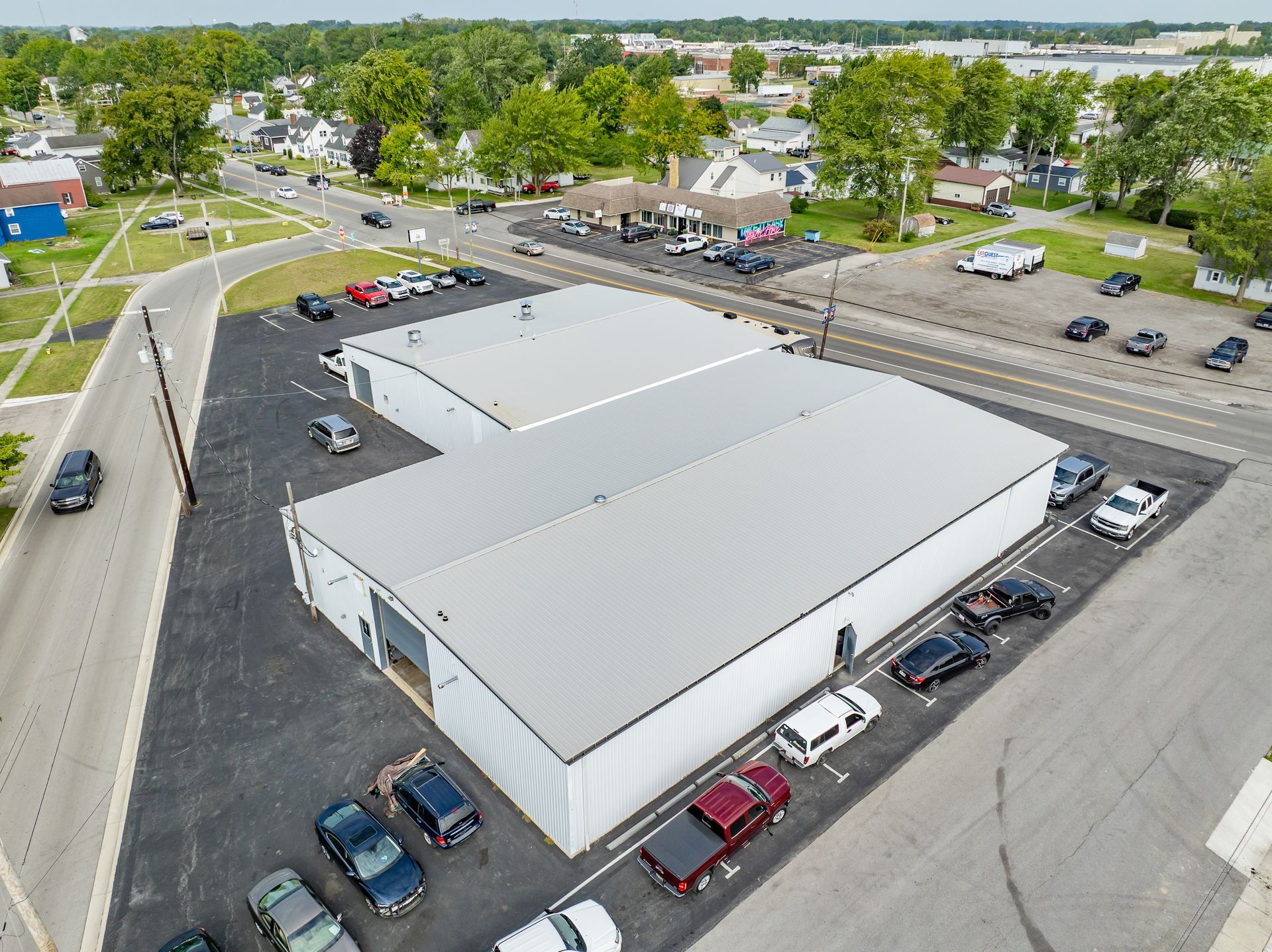 Aerial view of a white-roofed commercial building with parked cars and surrounding streets.
