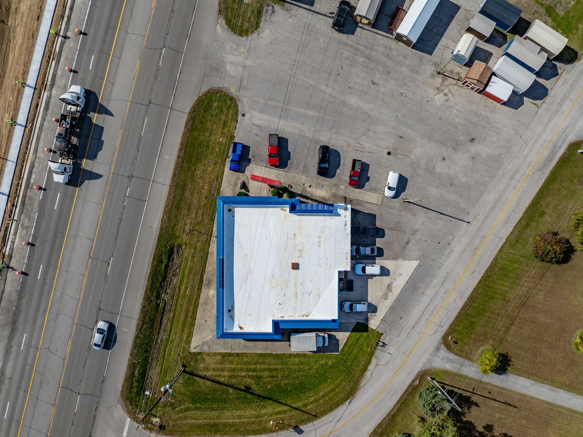 Aerial view of a white-roofed building with parked cars beside roads and grassy areas