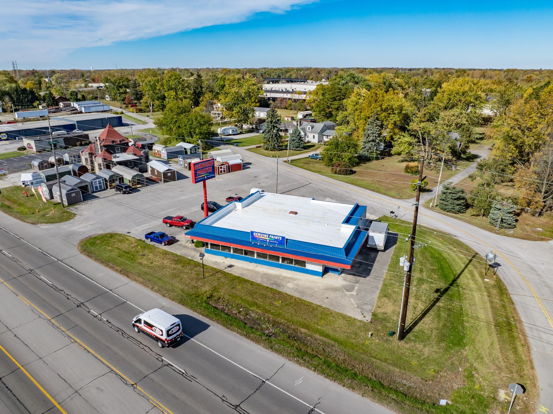 Aerial view of a blue-roofed commercial building beside a road, with trees and parking lot nearby.