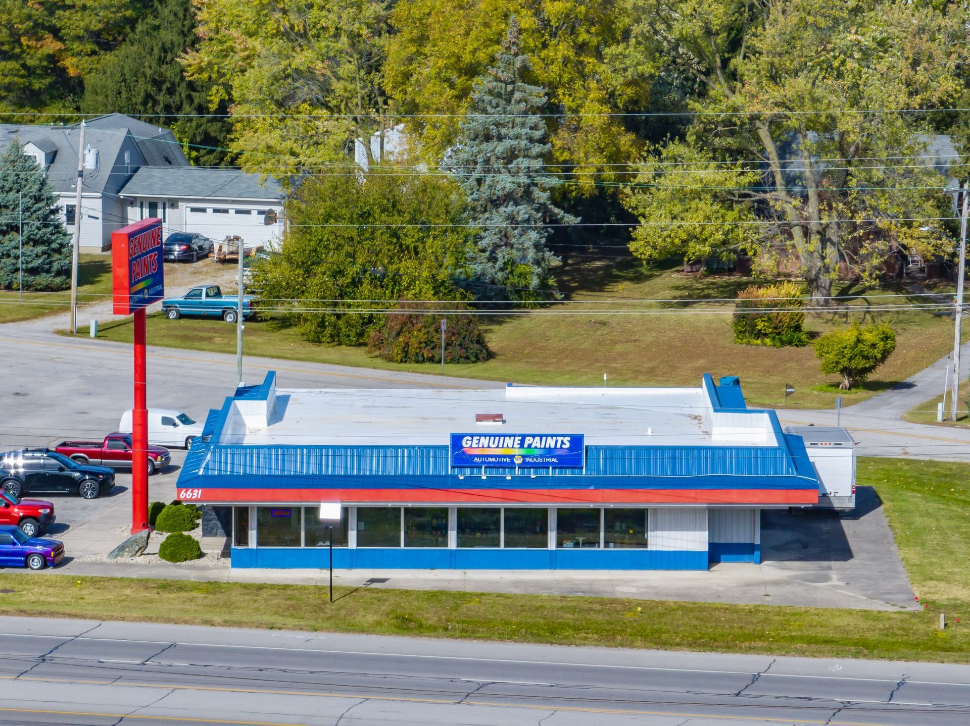 Motel-style building with blue and red roof beside a road and trees on a sunny day