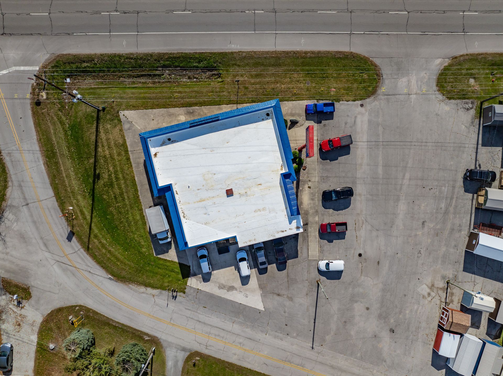 Aerial view of a blue-roofed building with parked trucks and cars in a lot beside a road.