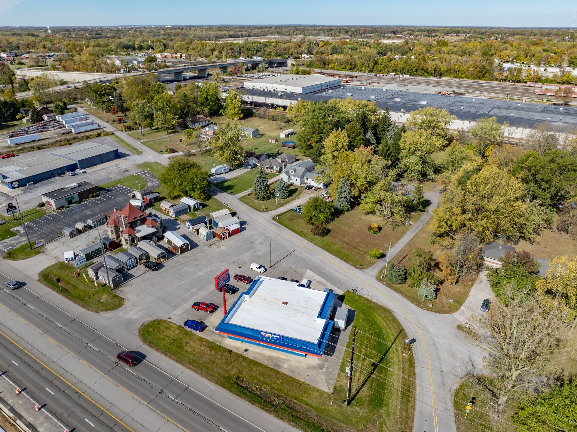 Aerial view of a roadside convenience store with a blue roof, parking lot, and surrounding trees.