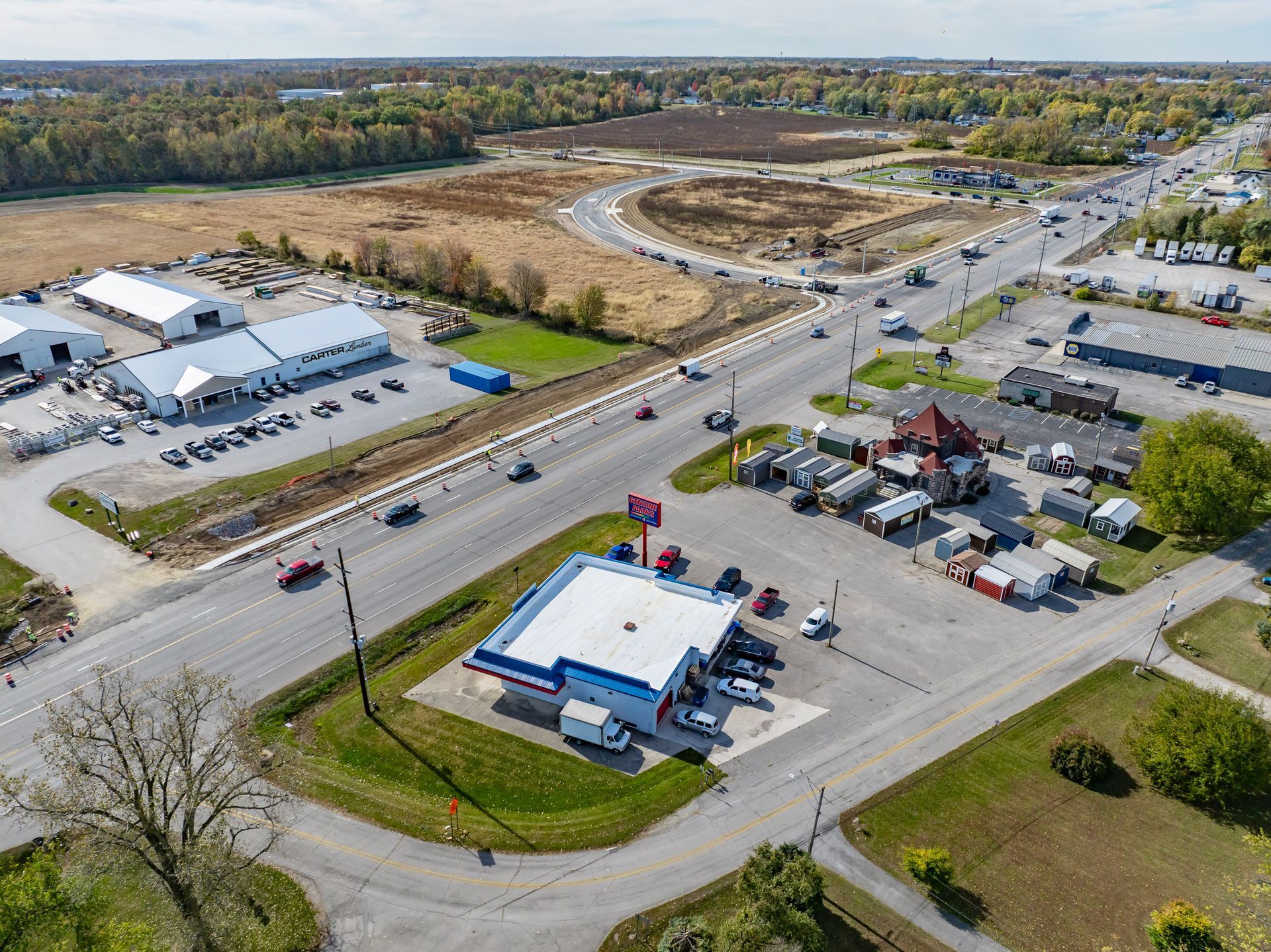 Aerial view of a roadside commercial area with parking lots, buildings, and an intersection near open land