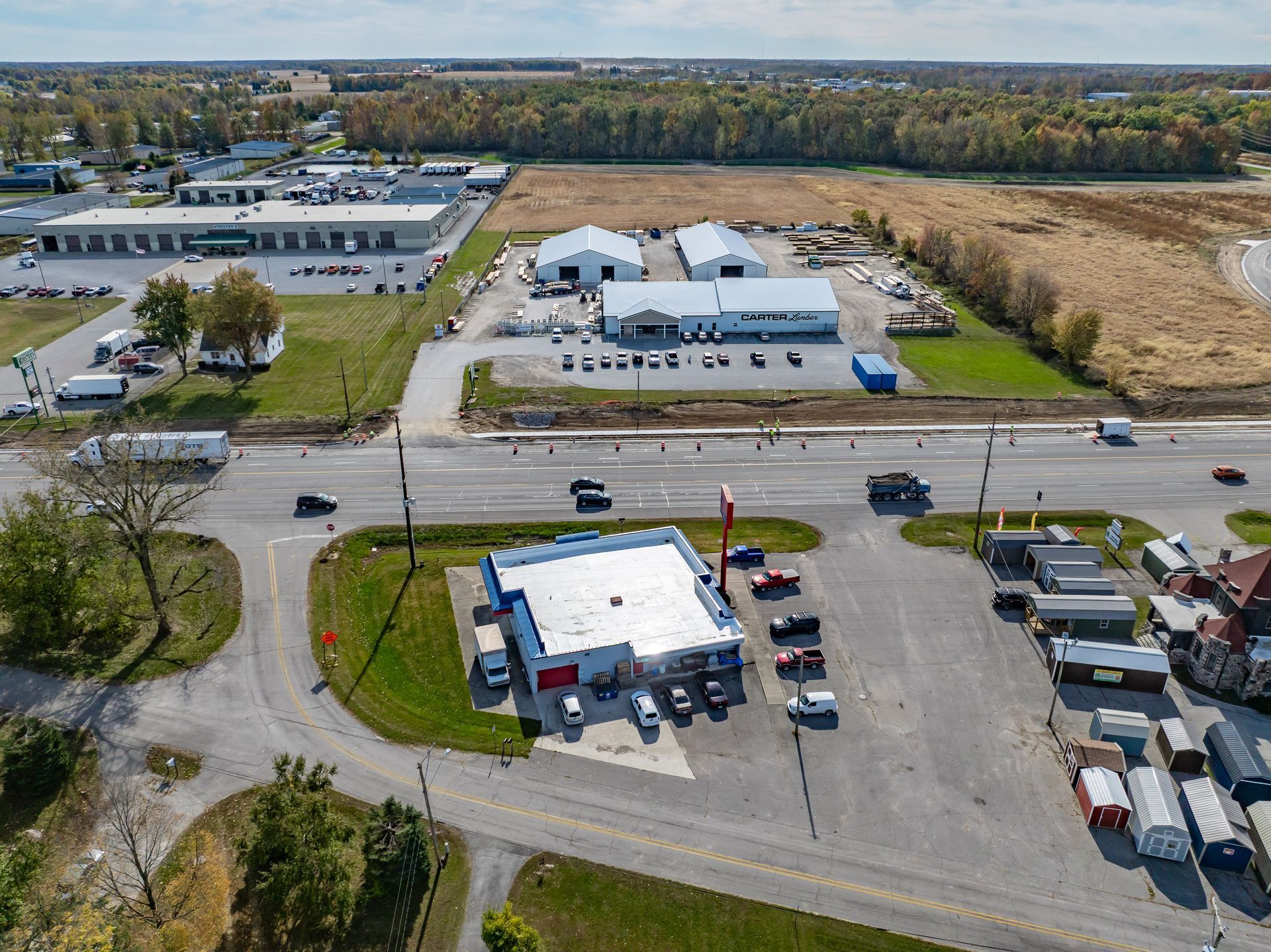 Aerial view of a roadside gas station and convenience store with parked cars near a highway.