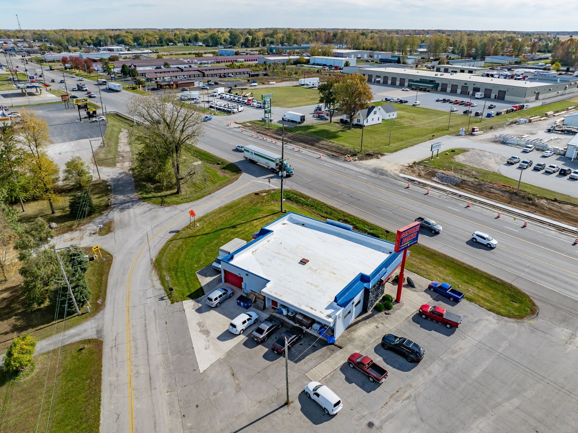 Aerial view of a gas station beside a busy road with cars and nearby commercial buildings.