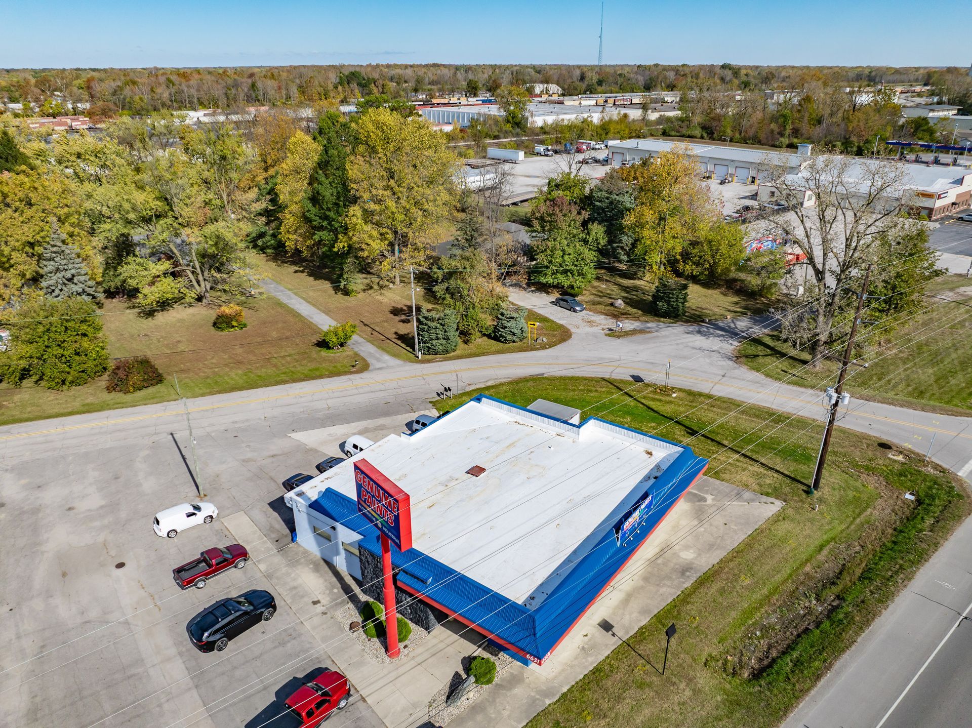Aerial view of a blue-and-white commercial building beside a road, with trees and parking lot nearby.