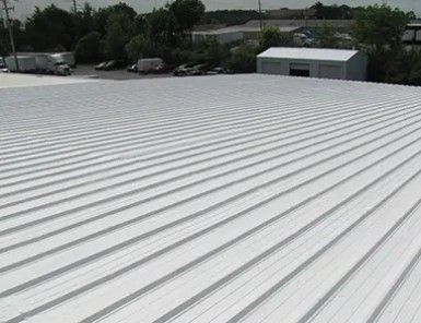 White corrugated metal roof on a building, with trees and small structures in the background.