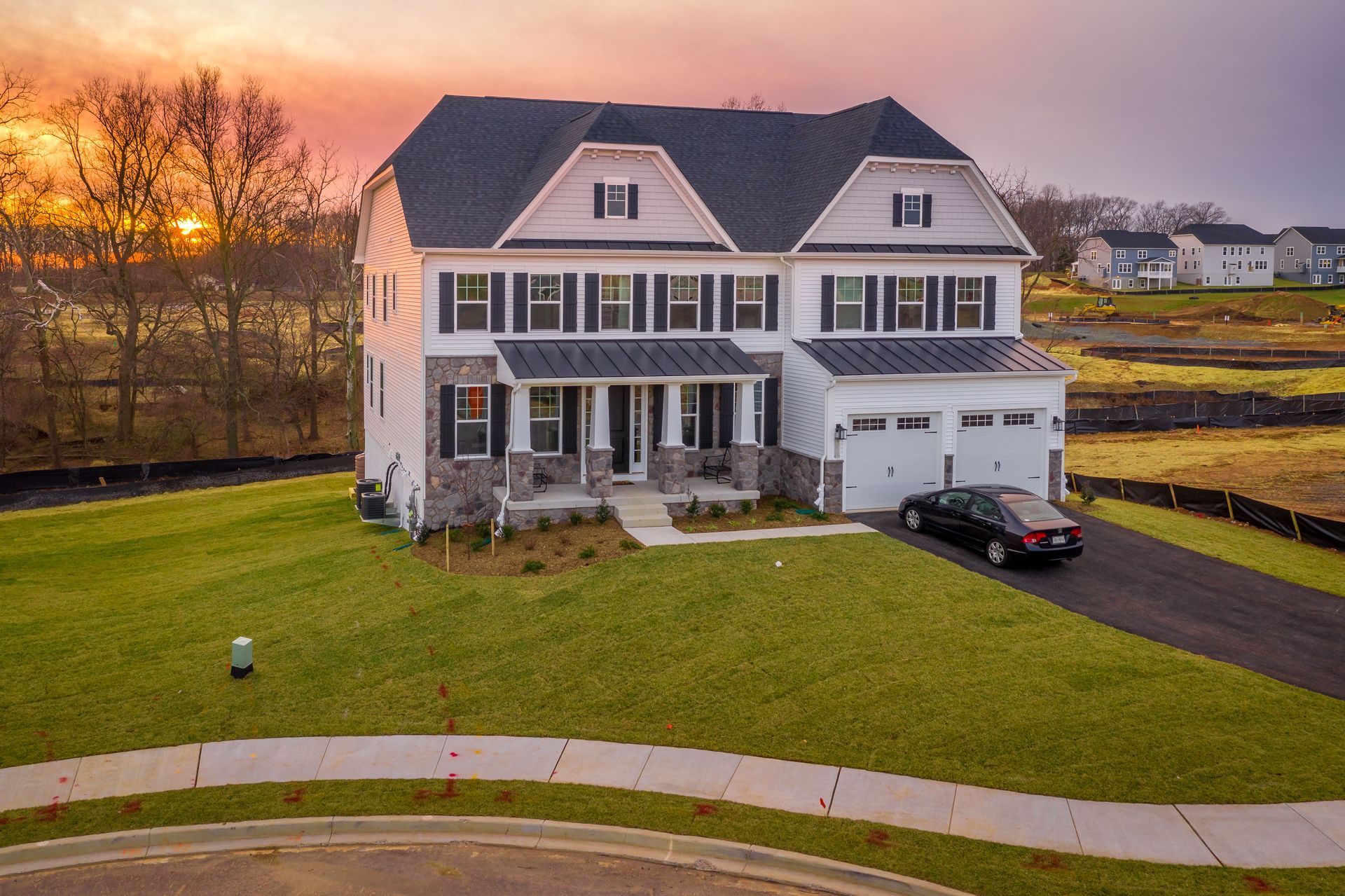 Large two-story suburban house at sunset with a front lawn, driveway, and parked car
