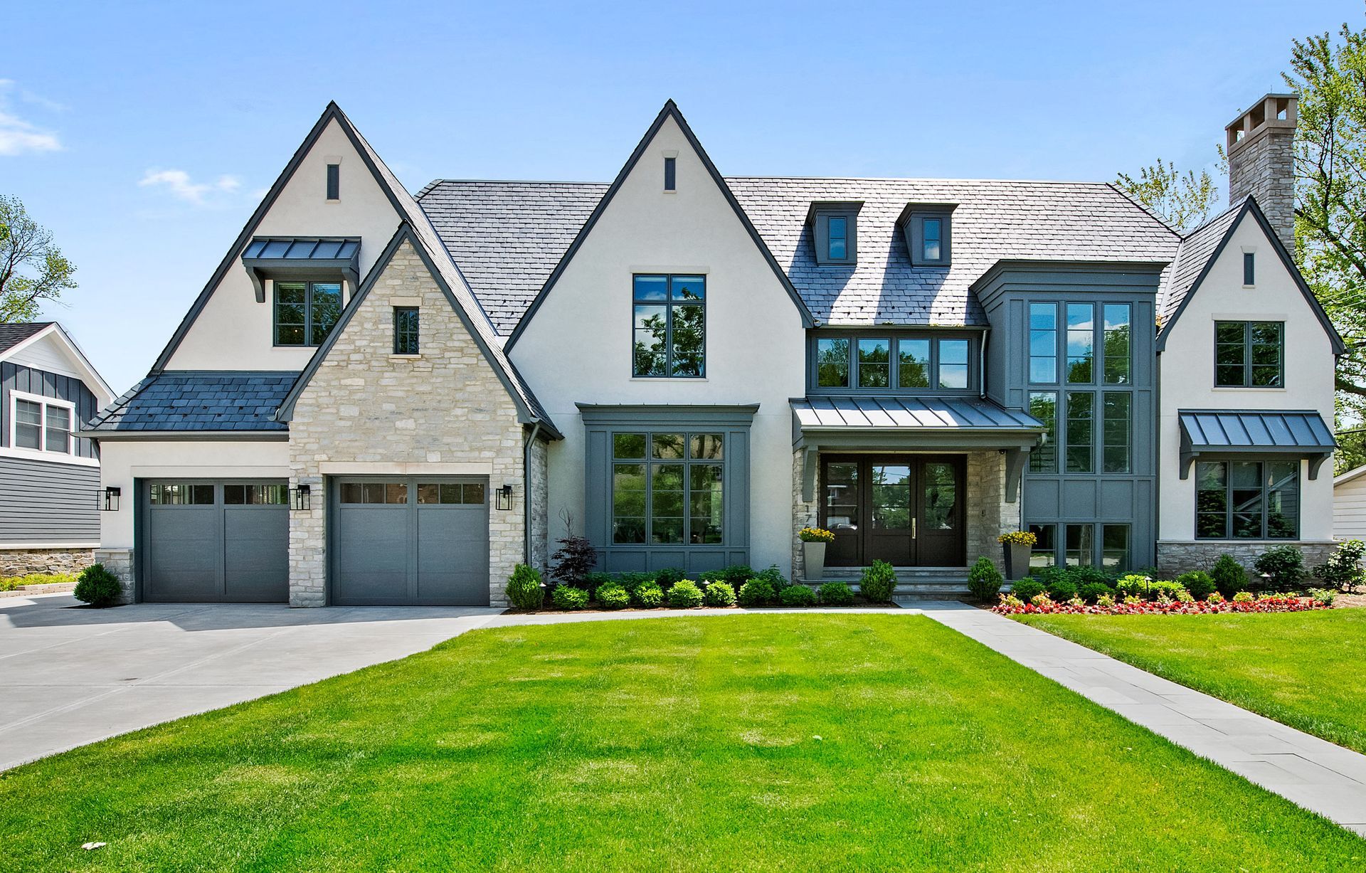 Large modern suburban house with stone and white siding, green lawn, and two-car garage