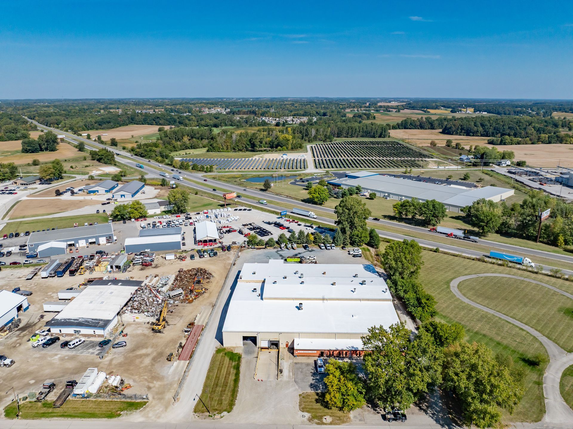 Aerial view of an industrial complex with warehouses, roads, and surrounding farmland under a clear blue sky