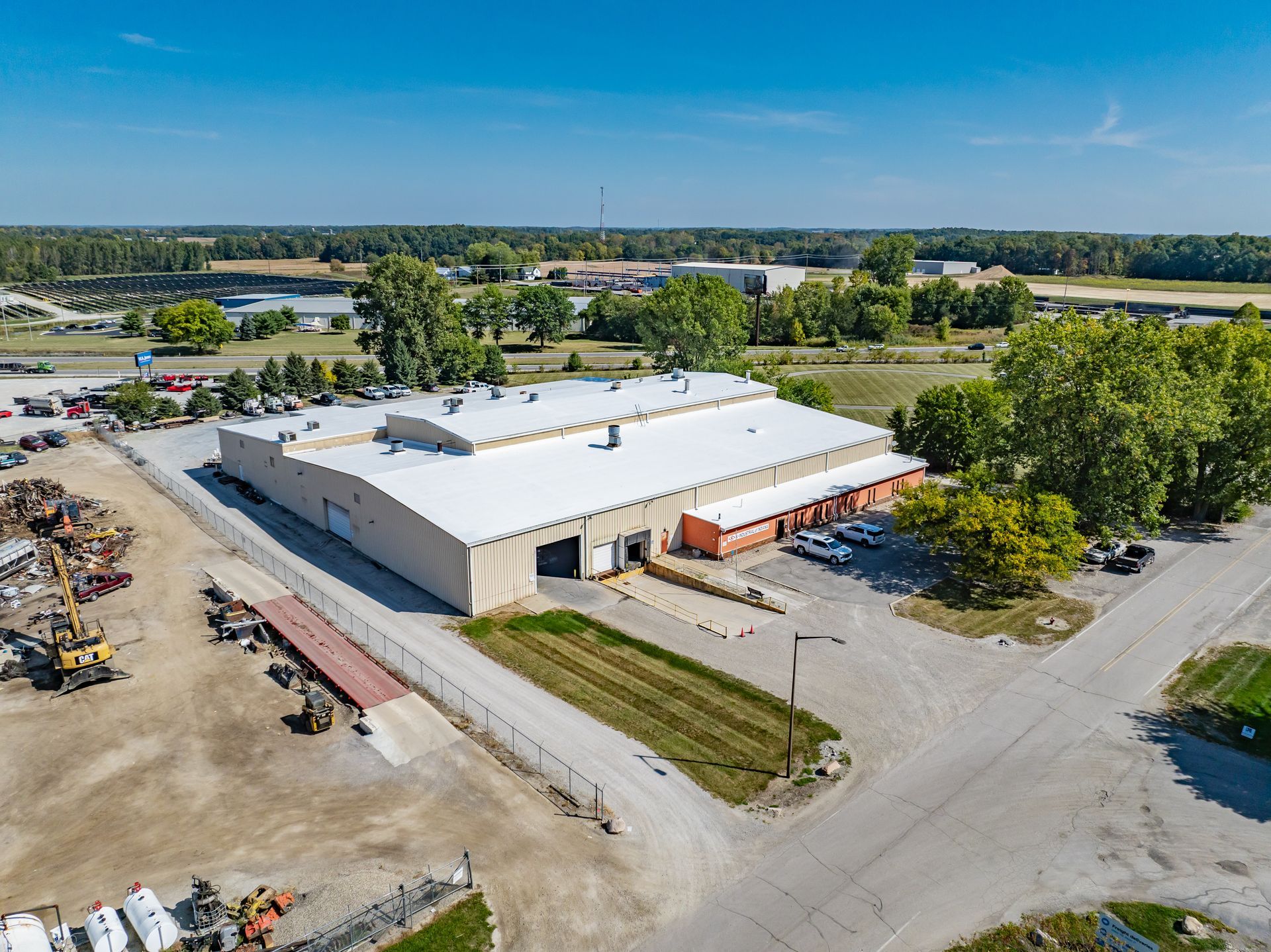 Aerial view of a large white industrial warehouse with loading docks and surrounding roads in a rural area