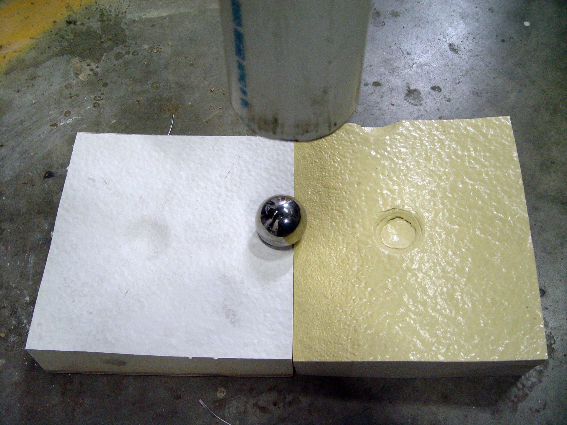 Metal ball bearing resting between a white and yellow block on a concrete floor