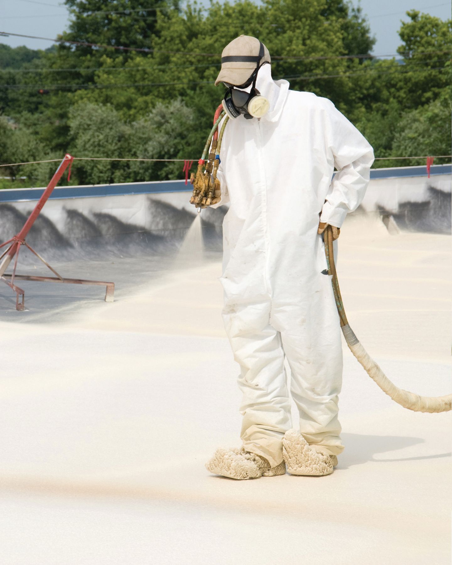 Worker in white hazmat suit spraying pesticide on a rooftop surface