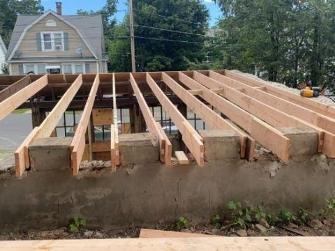 A roof is being built with wooden beams and a house in the background