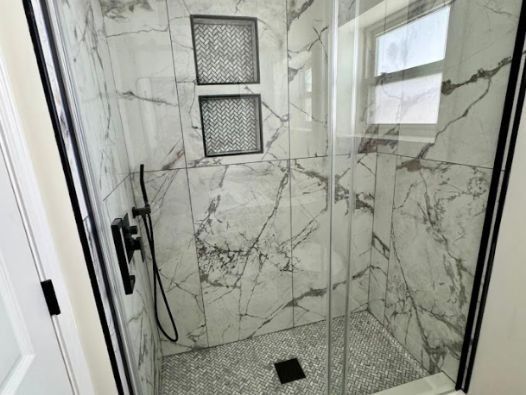 A bathroom with marble tiles and a walk in shower with a glass door.