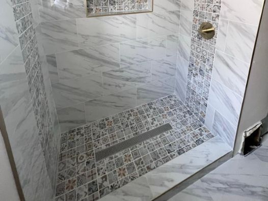A walk in shower with a tiled floor and a glass door.