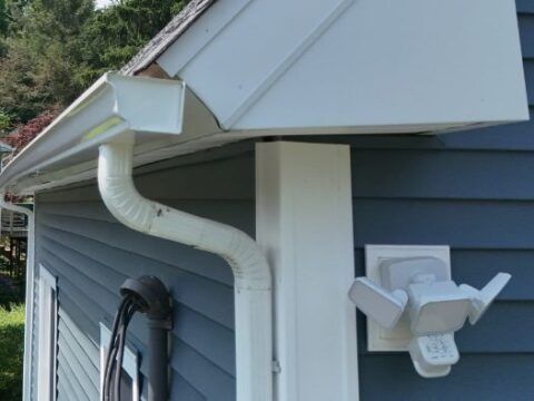 A blue house with a white gutter and a white light on the side.